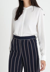Witte blouse met lange mouwen, een bandkraag en een knoopsluiting aan de voorkant, gecombineerd met marineblauwe en witte gestreepte hooggetailleerde broek met een getailleerde pasvorm.