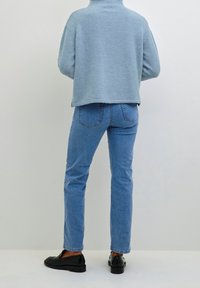 Světlounce modrý krátký svetr s vysokým límcem, doplněný středně modrými džínami a černými slip-on botami. Jednoduchý design bez viditelných vzorů.