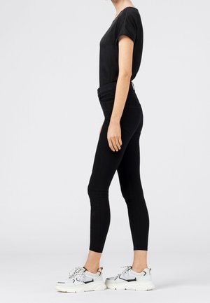 Jeans ajustados negros con cintura alta, combinados con una camiseta negra de manga corta y zapatillas blancas. Textura suave, diseño minimalista.