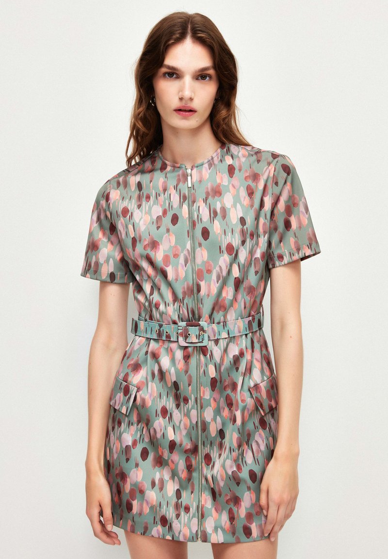 Robe à manches courtes avec une fermeture éclair en vert muted, présentant un motif de points multicolores, une taille ceinturée et deux poches avant.