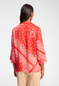 Rote gemusterte Bluse mit drei Viertelärmeln, ausgestattet mit weißen Blumen- und Paisleymustern, aus leichtem Stoff und mit lockerer Passform.