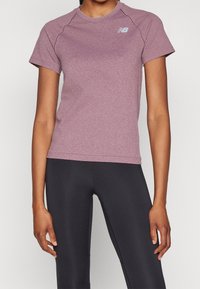 Kortärmad atletisk topp i melerad lila tyg med rund halsringning och diskret New Balance-logotyp, kombinerad med svarta leggings.