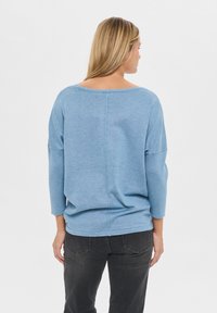 Jasnoniebieski sweter o szerokim dekolcie, z rękawami do trzech ćwiartek i luźnym krojem. Teksturowana tkanina i detale wzdłuż środkowego szwu pleców.