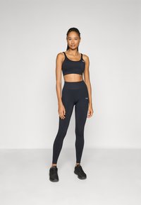 Black athletic crop top and high-waisted leggings, made of stretchy fabric, featuring a logo detail. Textured finish; paired with black sneakers.
