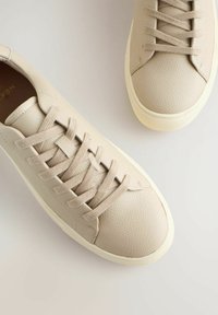 Beige leather sneakers with textured upper, flat laces, and a cream rubber sole. Smooth toe cap and minimalistic design.