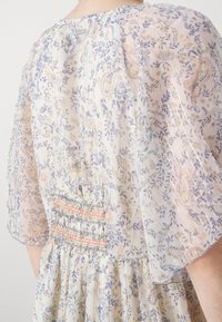 Lehká, průsvitná šaty s květinovým vzorem v pastelových barvách, krátkými, splývavými rukávy a smockováním na zadní straně.