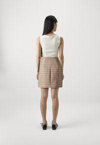 Top a righe bianche con una gonna beige caratterizzata da un motivo a diamante e pieghe. La modella indossa scarpe nere, vista da dietro.