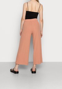 Pantalon large rose clair avec un design texturé en côtes et une taille élastique, associé à des sandales plates noires.