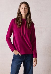 Felpa con cappuccio fucsia in tessuto a coste e con coulisse. Maniche lunghe abbinate a jeans in denim scuro. Design minimalista con vestibilità rilassata.