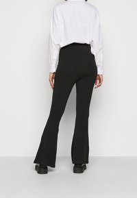 Svarta utsvängda byxor gjorda av mjukt tyg, med hög midja, slät yta och en diskret stretch för komfort.