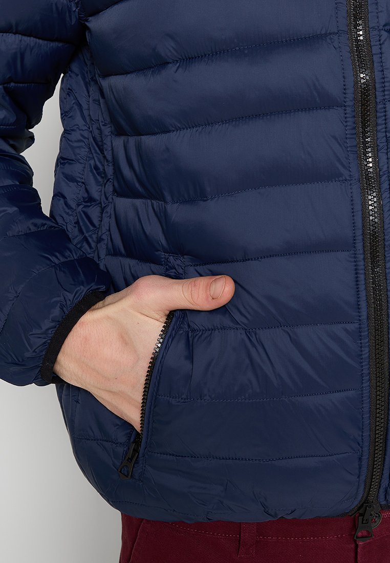 Chaqueta de plumas navy con diseño de acolchado horizontal, frontal con cremallera y bolsillos para las manos. El material parece suave y ligero.