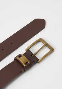 Ceinture en cuir marron avec une boucle en laiton rectangulaire, détail de couture et plusieurs trous d'ajustement. Texture lisse avec une extrémité effilée.