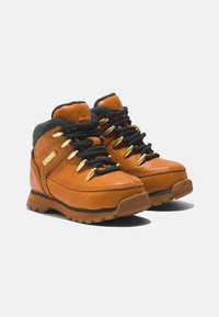 Botas de senderismo de cuero marrón con cordones negros, herrajes dorados y suela de goma. Cuentan con un collarín acolchado y un logotipo en relieve en el lateral.