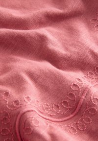Tessuto rosa morbido con delicate boucle e curve ricamate, che mostra morbide pieghe e dettagli della trama.