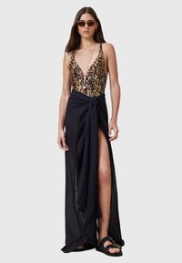 Badklänning med leoprint och djup ringskärning, matchad med en svart omslagskjol med hög slits och spetsdetaljer, stylad med sandaler.