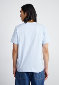 Lyseblå bomulds T-shirt med klassisk rund hals, korte ærmer og en glat tekstur, set fra ryggen. Simpelt design.