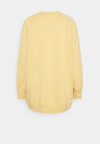 Felpa gialla in cotone con maniche lunghe a raglan, scollatura rotonda e orlo leggermente curvo nella parte inferiore. Nessuna grafica o motivo visibile.