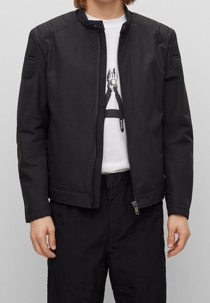 Black bomber jacket with a zip front, padded shoulders, and ribbed collar detailing. Paired with a white t-shirt and black pants.