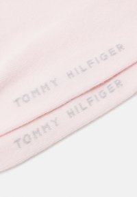 Chaussettes rose clair en tissu doux, avec "TOMMY HILFIGER" imprimé en gris sur le revers, à la texture lisse.