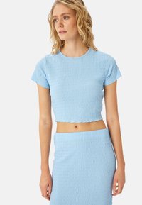 Top corto azul claro hecho de tejido texturizado con mangas cortas y cuello redondo, combinado con una falda entallada a juego.