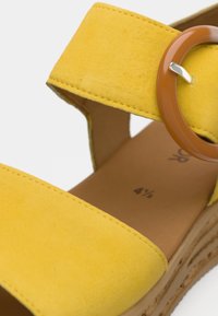 Κίτρινο σανδάλι από σουέτ με φαρδιά λουράκι, στρογγυλή καφέ αγκράφα και καφέ σόλα με ανάγλυφη υφή σε στρώσεις.