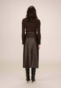 Gonna midi in pelle marrone con texture liscia e linee pulite, abbinata a un maglione aderente in maglia rigata marrone e stivali neri con tacco.