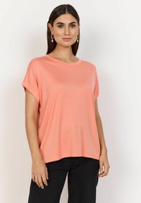Haut rose saumon à manches courtes avec un col rond, coupe décontractée et texture côtelée douce. Associé à un pantalon noir.