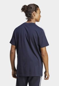 Tamnoplavi pamučni T-shirt s kratkim rukavima i okruglim izrezom, s bijelim bočnim trakama i opuštenim krojem. Stražnji pogled prikazuje glatku teksturu.