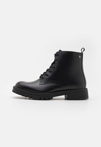 Botas negras de tobillo hechas de cuero suave, con un diseño de cordones, puntera redonda, detalles en relieve y suelas de goma gruesa con tacos.