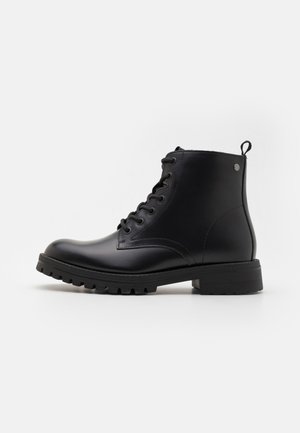 Botas negras de tobillo hechas de cuero suave, con un diseño de cordones, puntera redonda, detalles en relieve y suelas de goma gruesa con tacos.