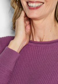 Lila gerippter Strickpullover mit Rundhalsausschnitt. Nahaufnahme einer Hand, die auf einem Hals ruht, mit Betonung auf der Hautstruktur und dem weichen Stoff.