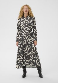 Langärmliges, knopfbares Kleid in Schwarz mit einem weißen abstrakten Muster, aus glattem Stoff. Mit einem taillierten Bund und langen Ärmeln.