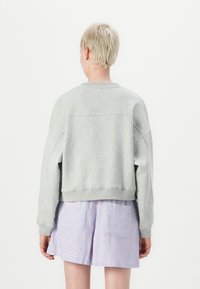 Sweatshirt court gris clair avec des épaules tombantes et un ourlet côtelé, associé à un short rayé taille haute en bleu et rose.