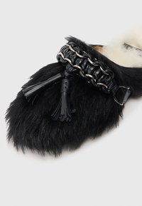 Pantof black cu blană, având vârful rotund, dotat cu o curea din piele neagră decorată cu un lanț metalic și ciucuri decorative.