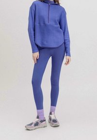 Lila fleecepullover med halvdragkedja, parat med matchande högmidjade leggings. Har texturerad tyg och lager på lager-sockor med sneakers.