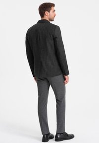 Blazer grigio a righe con tessuto testurizzato e rever a punta. Abbinato a pantaloni tapered grigi coordinati e scarpe nere.