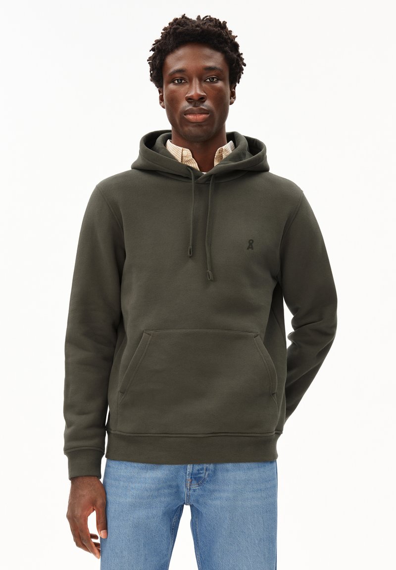 Felpa verde oliva realizzata in tessuto morbido, con tasca frontale e coulisse, con un piccolo logo sul petto. Indossata sopra una camicia a quadri.
