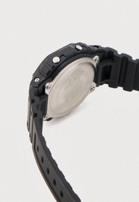 Mustast kummist spordikell tekstureeritud rihmaga, hõbedaste detailidega ja roostevabast terasest tagaküljega. Kellal on nähtavad kruvid ja veekindluse märgistus.