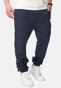 Marineblaue Baumwoll-Sweatpants mit tiefem Schritt, elastischen Bündchen und Seitentaschen, kombiniert mit weißen Sneakern.