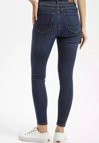 Slim fit jeans z ciemnego denimu o gładkiej teksturze, pięcioma kieszeniami, szlufkami na pasek i subtelnymi detalami szycia, w zestawieniu z białymi sneakersami.