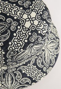 Cappello a secchiello nero e crema con motivi floreali e geometrici intricati, realizzato in tessuto strutturato con una parte superiore arrotondata.