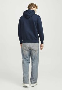 Marineblå pullover hoodie med en snor i hætten, i en bomuldsblanding, med ribbede manchetter og kant; båret med lyse vaskede, afslappede jeans og hvide sneakers.