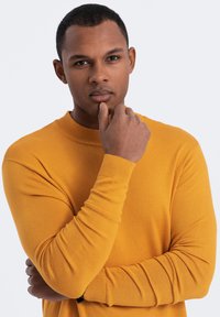 Mustard yellow knitted sweater with a ribbed neckline and cuffs, featuring a close-fitting design and a smooth texture.