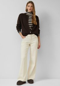 Brązowy dziergany kardigan z dekoltem w serek i guzikami, podkoszulek z golfem w paski, kremowe spodnie o szerokich nogawkach oraz ciemnobrązowe buty. Całość ma gładką teksturę.