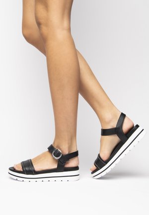 Black leather sandals with two straps and adjustable buckle. Thick white sole with textured black accents, featuring a small cutout design.