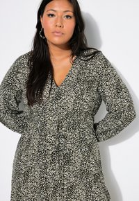 Schwarz-weißer, gemusterter Kleid mit langen Ärmeln, V-Ausschnitt und einer Kordelzug-Taille. Der Stoff hat eine strukturierte Optik.