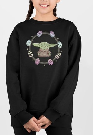 Sort sweatshirt med en centreret tegneseriefigur med store ører, omringet af farverige påskeæg i et cirkulært design.