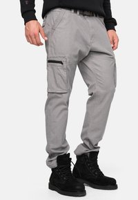Pantalon cargo gris avec plusieurs poches, détails zippés et coupe décontractée, associé à des bottes à lacets en daim noir.