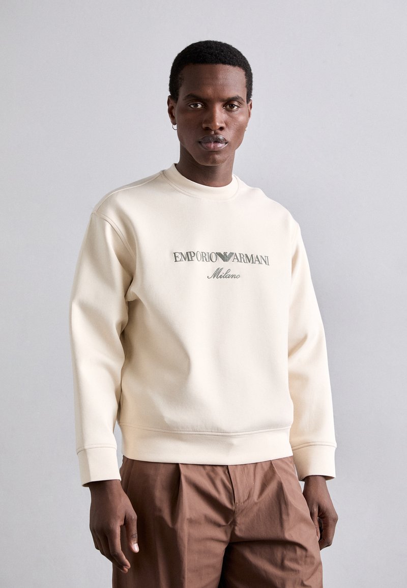 Crème sweatshirt met een ronde hals, voorzien van een geborduurd 'Emporio Armani Milano' logo. Oversized pasvorm met ribgebreide manchetten, gecombineerd met een paarse broek.