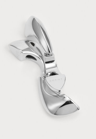 Stilren metallhårklämma i glänsande silver, med en slät, böjd design och en triangulär logotypdetalj samt intrikata detaljer.